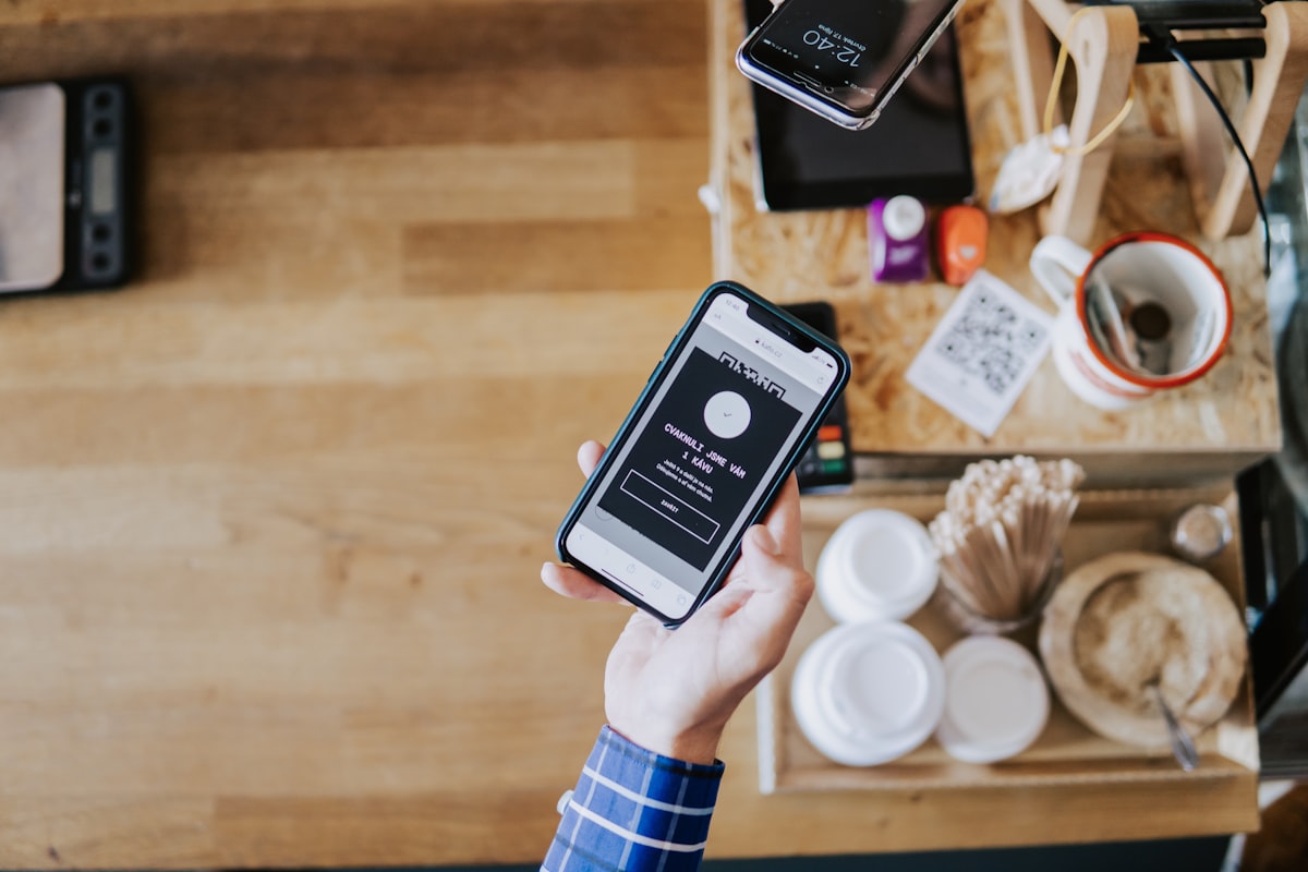 Hand hält Smartphone über einem Cafétresen